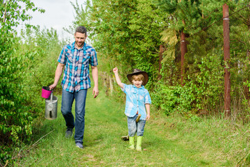 Fototapeta premium Ready to work. father and son in cowboy hat on ranch. Eco farm. small boy child help father in farming. use watering can and pot. Garden equipment. happy earth day. Family tree nursering