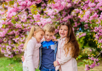 Happy spring vacation. Girls and boy friends posing near sakura. Kids on pink flowers of sakura tree background. Kids enjoying cherry blossom sakura. Children enjoy warm spring. Lost in blossom