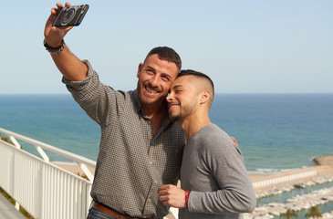 Una pareja gay se hace un selfie en el balcón de su casa en un día de verano con el puerto detrás