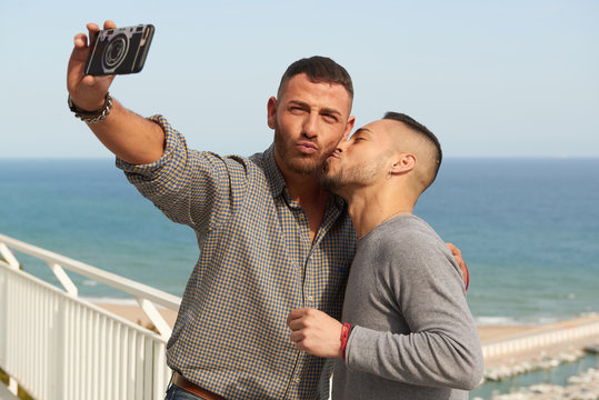 Una pareja gay se hace un selfie en el balc&oacute;n de su casa en un d&iacute;a de verano con el puerto detr&aacute;s