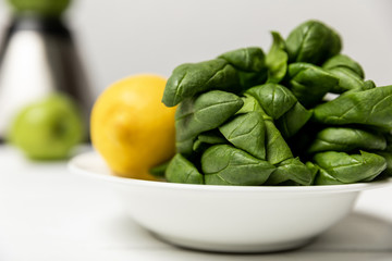 selective focus of green fresh spinach leaves near yellow lemon on white