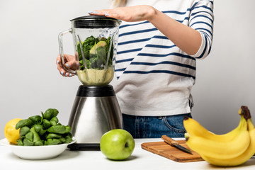 cropped view of woman using blender near fruits on white