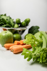Obraz na płótnie Canvas selective focus of celery near carrots, ripe apple and green vegetables on grey