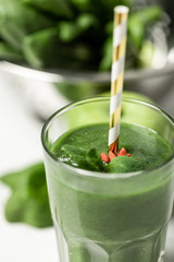 selective focus of tasty green smoothie in glass with straw near spinach leaves on white