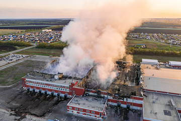 Burning industrial building with fire, huge thick smoke and burnt roof, aerial view from drone