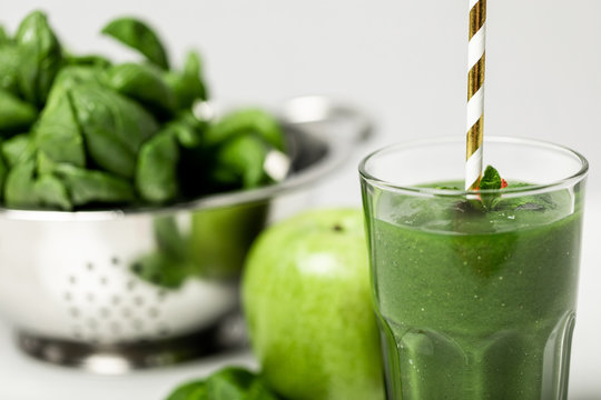 Selective Focus Of Tasty Green Smoothie In Glass With Straw Near Spinach Leaves And Apple On White