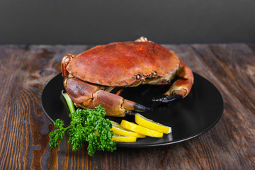 Cooked crabs on black plate served with fresh lemon and parsley, wooden background, top view.