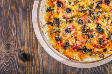 Top view of Italian PIZZA with meat tomato, olives and cheese. Dark wooden table background. Close up