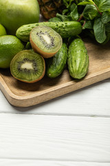 halves of tasty ripe kiwi fruit near cucumbers on wooden cutting board