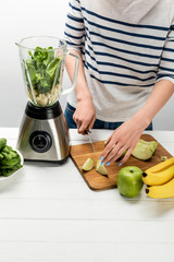 cropped view of woman cutting organic apple near blender with ingredients on white