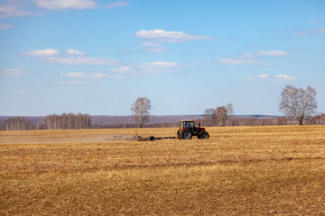 Fototapeta premium Red tractor with a trailed plow for mowing and weeding fields for the agro-industry of yellow color under the blue sky, a clear spring day. Preparation for planting crops rural technology. Farming.