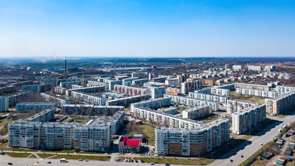 spring landscape from a aerial view of the small city of Leninsk Kuznetsk, of the streets with a road, tall buildings, houses with roofs under blue sky, parking lots, cars, trees.