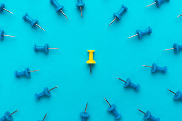 yellow push pin in the center of blue push pins with their spike turned to the yellow one as a...