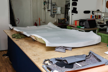 Gray ceiling lining removed from the car for tuning and bracing with grey soft material on a table in the workshop on the background of tools and equipment for working with the interior of vehicles