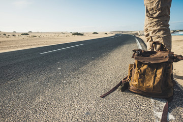 Travel people and adventure lifestyle concept with closeup of man standing on the long road with trendy backpack waiting for a car to share the trip - beautiful desert natural outdoor around