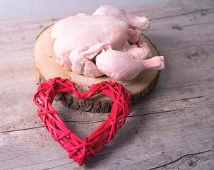 Raw chicken next to a heart on wooden table. Food