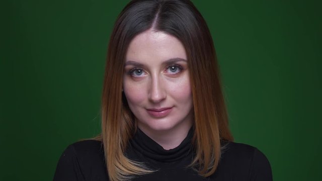 Portrait of young businesswoman with chestnut hair smiling modestly into camera on green background.