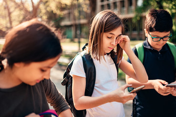 Schoolgirl with allergy rubbing eye and using smart phone