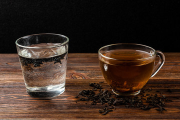 Cup of black tea and water on dark wooden background.