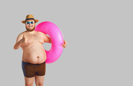 Fat funny man in swimming trunks with an inflatable ring on a gray background.