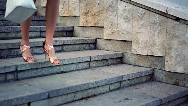 Girl runs on steps down on high heels stiletto in street city outdoor. Side low angle by legs and shoes summer sandals also border of white dress.
