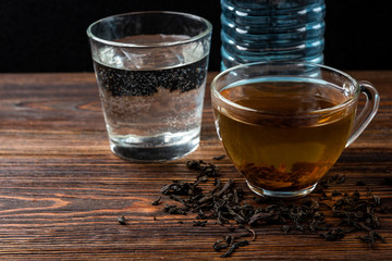 Cup of black tea and water on dark wooden background.