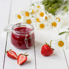 Strawberry jam in a glass jar on a table with chamomiles