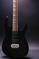 Body and neck of electric guitar. Close up detail. Accentuated shapes by illumination. With copy space on dark backgrouna