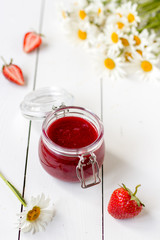 Strawberry jam in a glass jar on a table with chamomiles