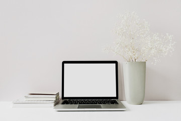 Minimalist home office desk workspace with laptop, flowers bouquet on pink background. Front view...