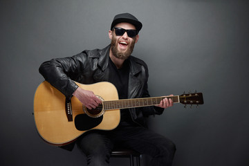 Guitar player singing in music studio. Hipster guitar player with beard and black clothes playing...