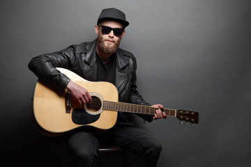 Guitar player singing in music studio. Hipster guitar player with beard and black clothes playing the acoustic guitar