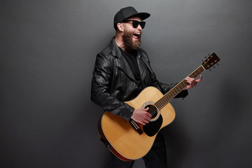 Obraz premium Guitar player singing in music studio. Hipster guitar player with beard and black clothes playing the acoustic guitar