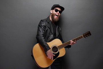 Obraz premium Guitar player singing in music studio. Hipster guitar player with beard and black clothes playing the acoustic guitar