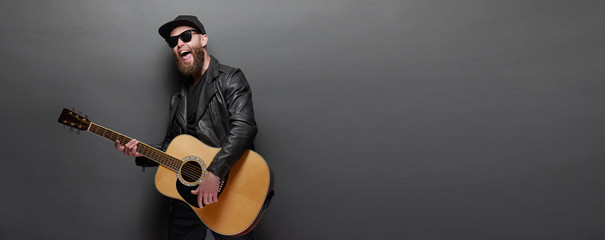 Guitar player singing in music studio. Hipster guitar player with beard and black clothes playing...