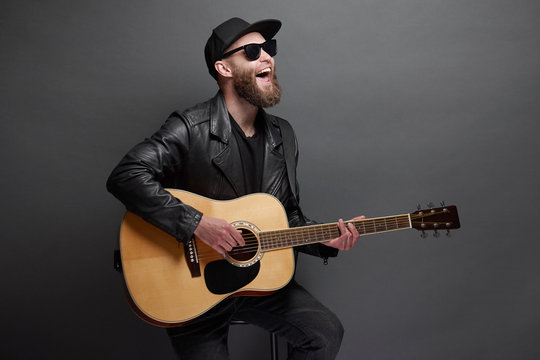 Guitar player singing in music studio. Hipster guitar player with beard and black clothes playing the acoustic guitar