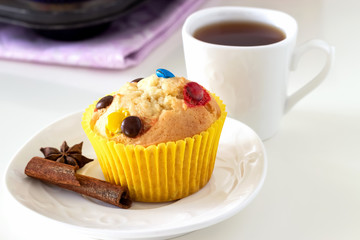 Homemade lemon muffins with colorful chocolate candy in paper case and cup tea. White background. Selective focus.