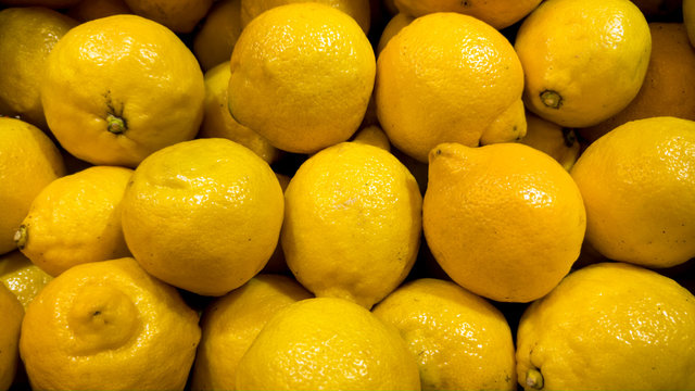 Closeup image of lots of organic lemons lying on store counter. Closeup texture or pattern of fresh ripe fruits. Beautiful food background