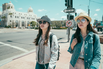 two young asian women tourist walking together on city street. female college friends classmates...