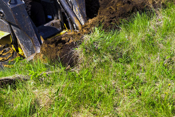 partial view of excavator bucket digging pit in grassy soil during earth works
