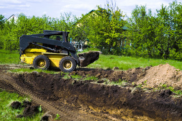 mini loader with grassy soil in bucket during earth works in countryside
