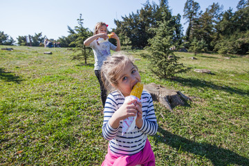 Two little girls eating boiled corn in the park