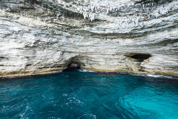 A boat going out of the marin cave with the stalactites on the top and turquoise water outside near Bonifacio. Corsica, France 2019.