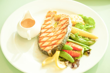 Grilled salmon with lemon and salad on white plate.