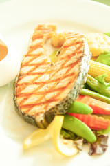 Grilled salmon with lemon and salad on white plate.