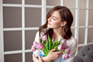 Young beautiful brunette girl holding a spring bouquet of tulips in her hands. Lifestyle