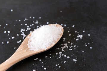 Fototapeta na wymiar white coarse edible salt on a wooden spoon on a black surface