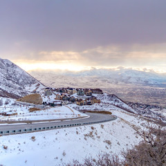 Clear Square Road curving along a mountain coated with snow against cloudy sky in winter