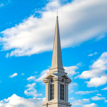 Square Exterior of a beautiful church with a white steeple against cloudy blue sky