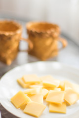 Semi-hard cheese sliced in white plate. Two wicker cups on a sunny table